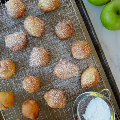 Apple fritters dusted with powdered sugar on a wire rack.