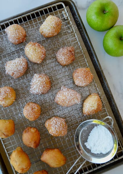 Apple fritters dusted with powdered sugar on a wire rack.