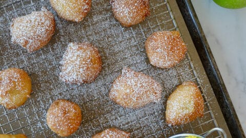 Apple fritters dusted with powdered sugar on a wire rack.