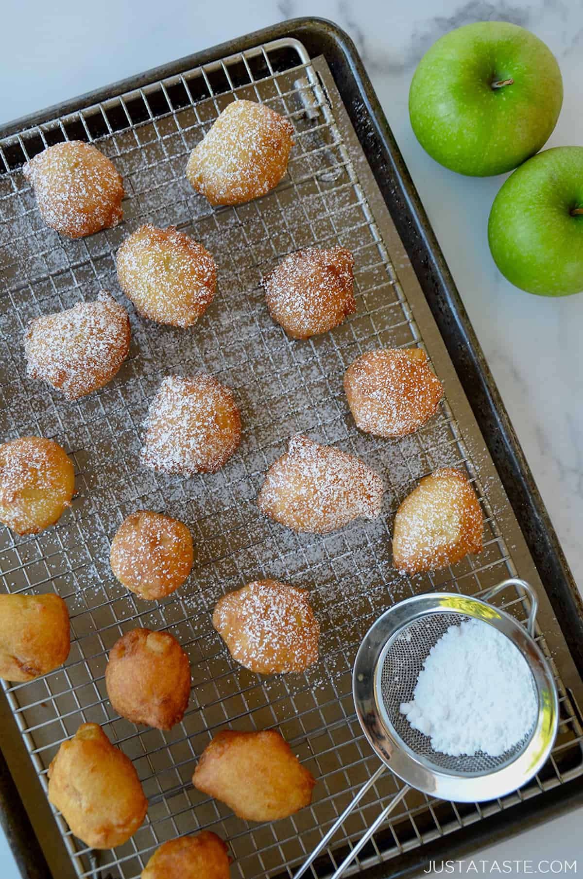 Apple fritters dusted with powdered sugar on a wire rack.