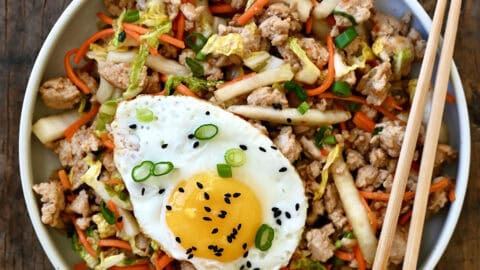 Egg roll in a bowl with ground meat, shredded cabbage and carrots, topped with a fried egg and black sesame seeds.
