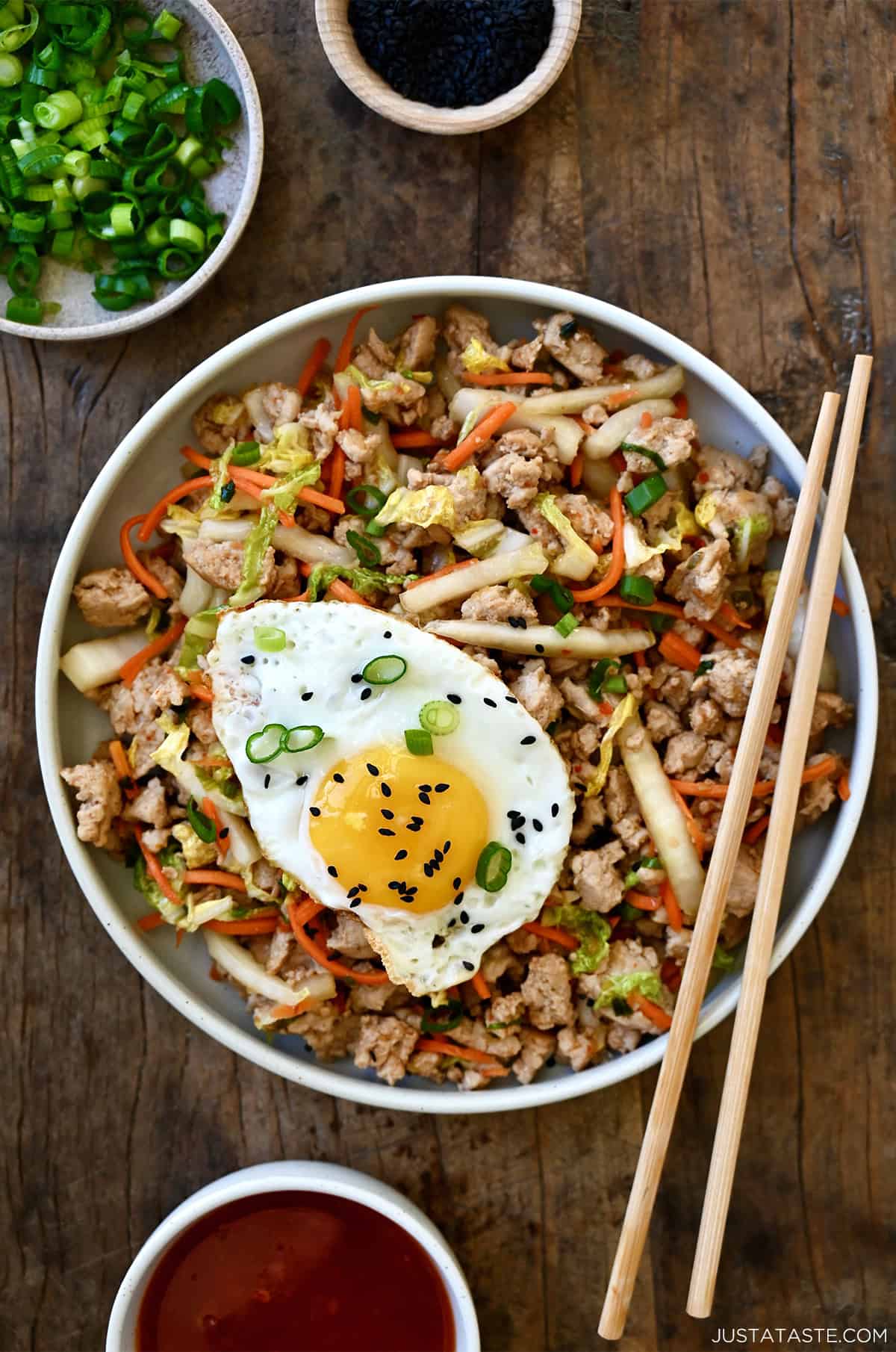 Egg roll in a bowl with ground meat, shredded cabbage and carrots, topped with a fried egg and black sesame seeds.