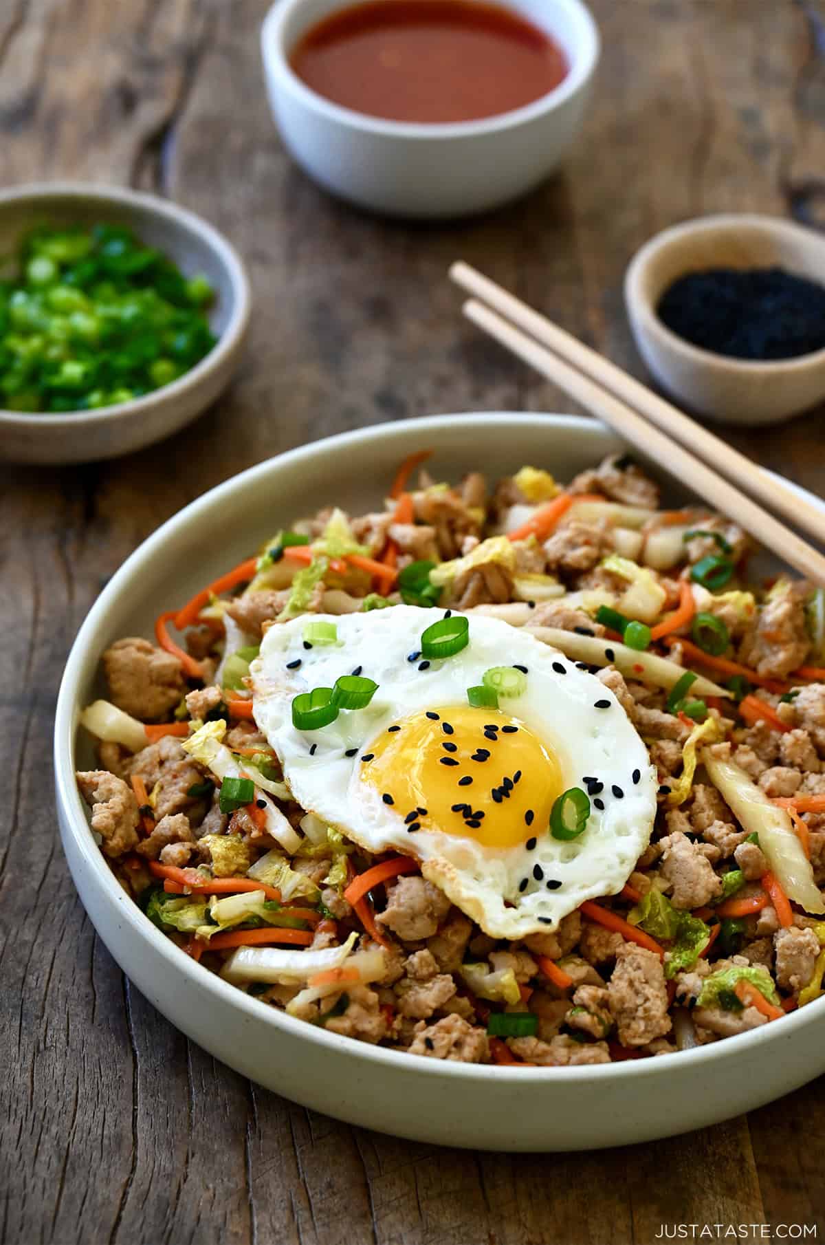 Healthy egg roll in a bowl, including ground turkey, coleslaw mix and soy sauce, topped with a fried egg and black sesame seeds.