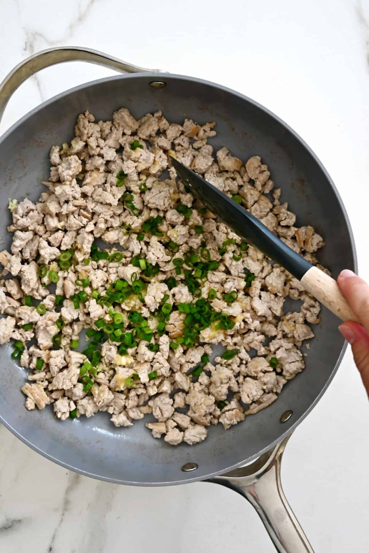 Chopped scallions, minced garlic and ginger atop browned meat in a skillet.