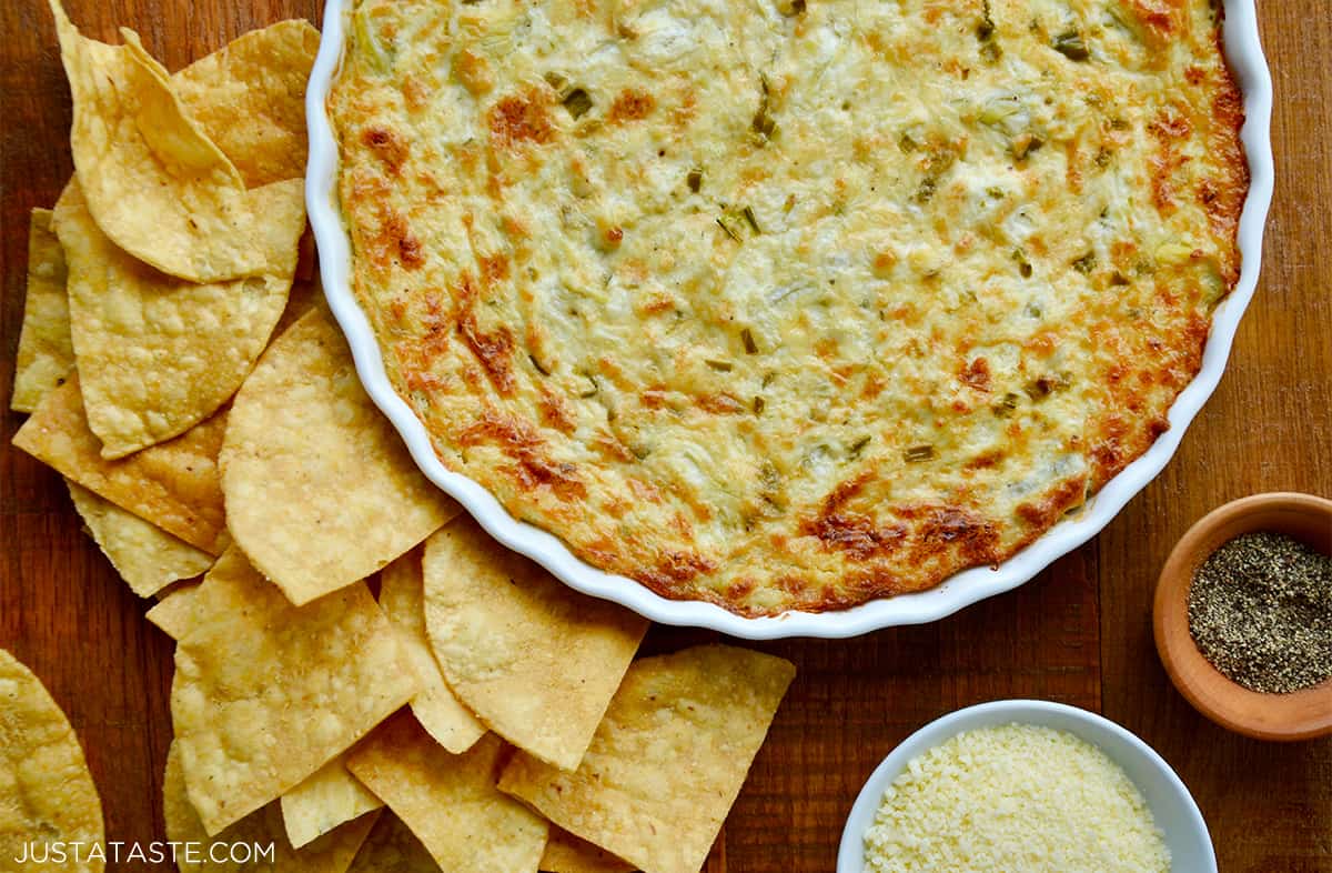 Tortilla chips surrounding a white baking dish containing hot and creamy artichoke dip.