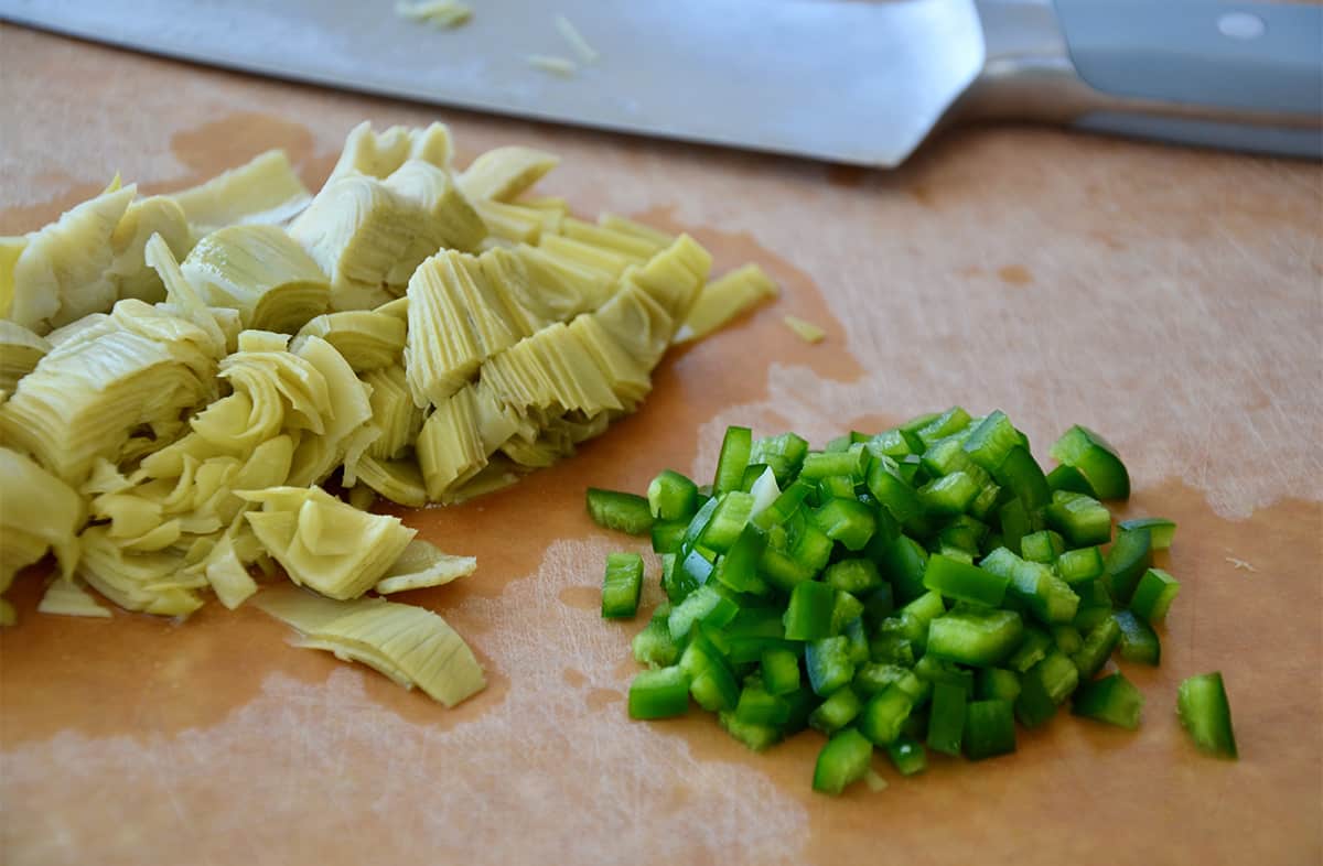 Chopped artichoke hearts and jalapeños on a cutting board next to a sharp knife.