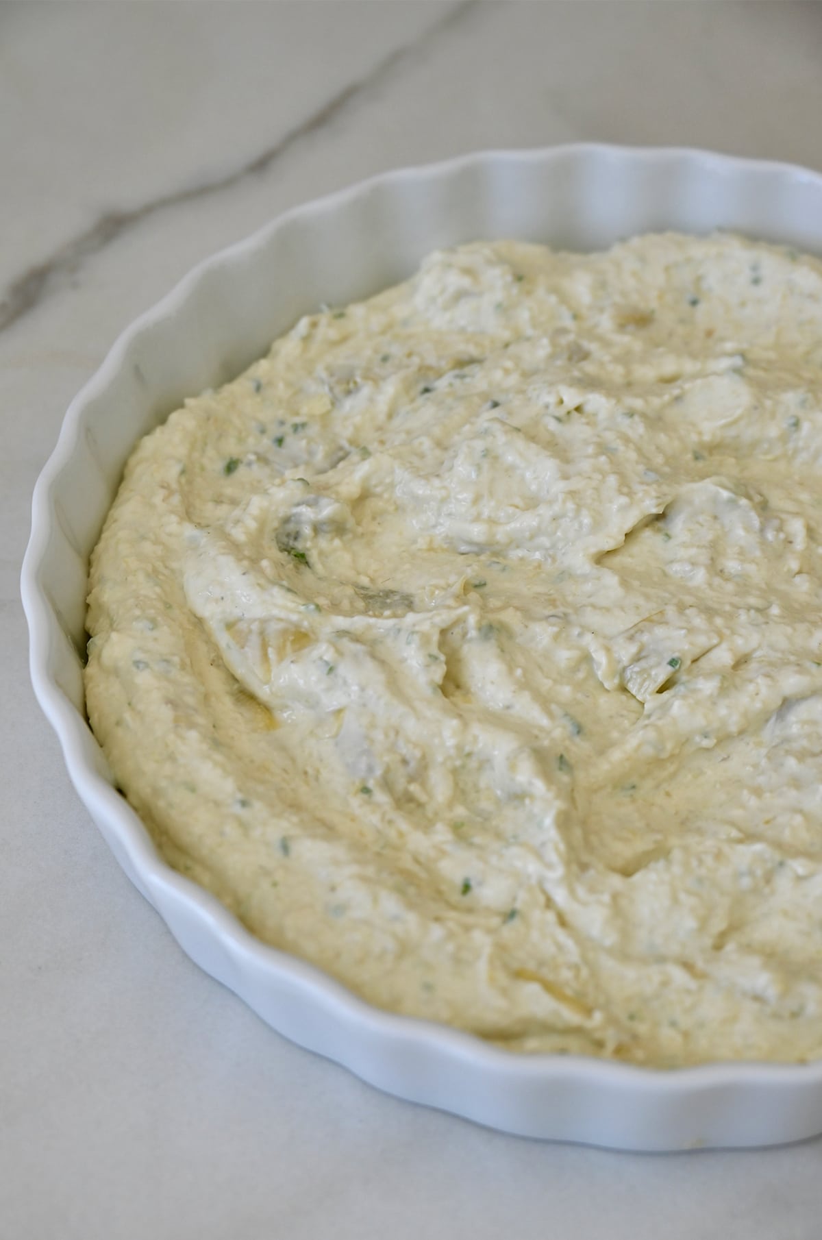 Unbaked artichoke dip in a shallow baking dish.
