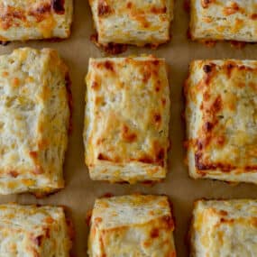 Rectangular cheddar biscuits are arranged in rows on brown parchment paper.