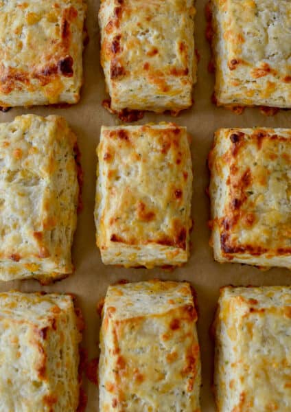 Rectangular cheddar biscuits are arranged in rows on brown parchment paper.