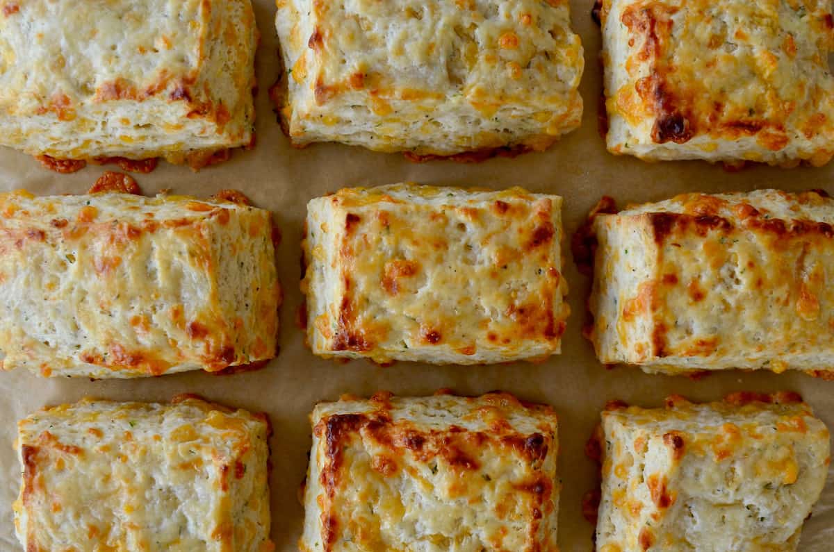 Rectangular cheddar biscuits are arranged in rows on brown parchment paper.