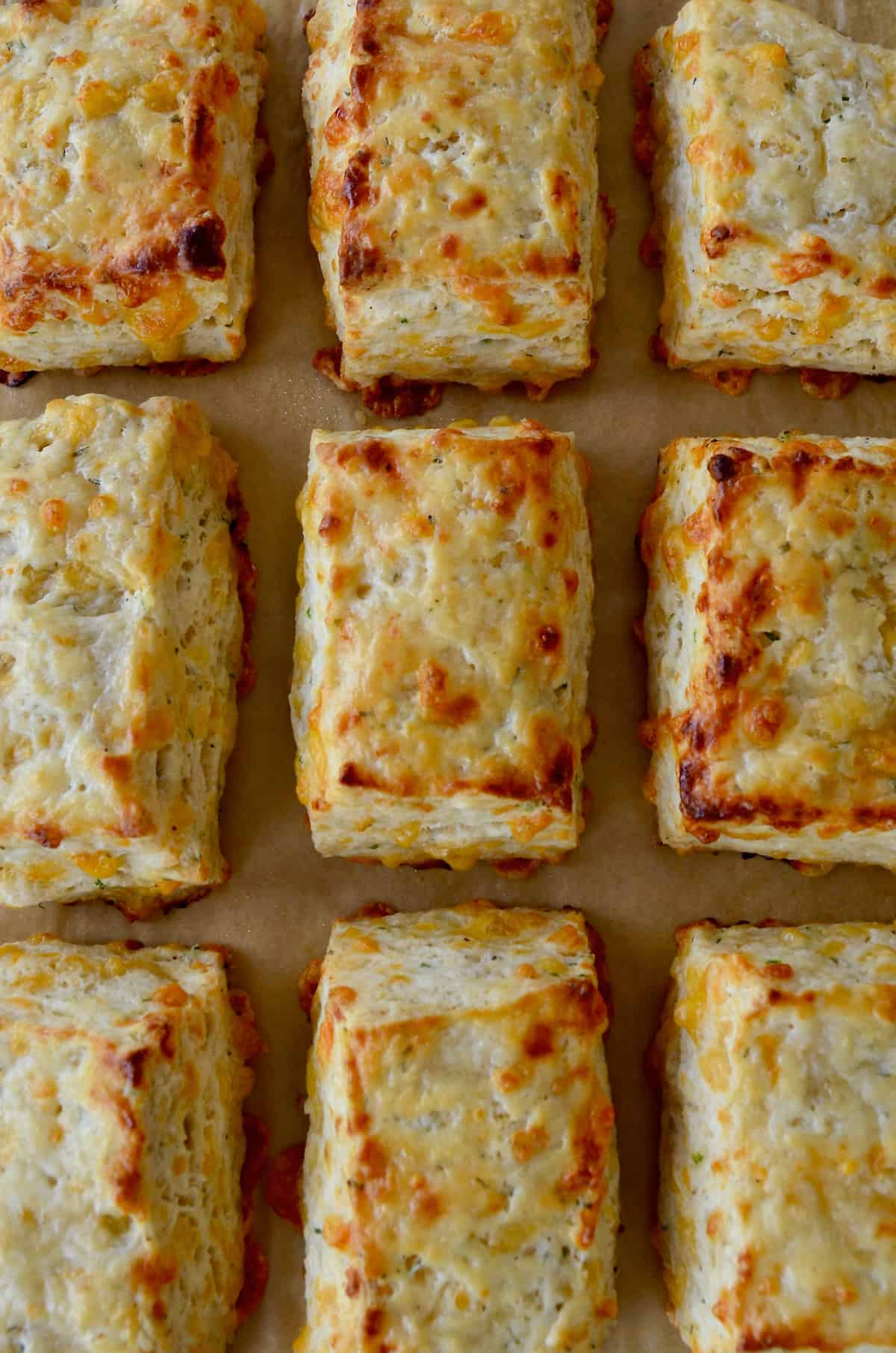 Rectangular cheddar biscuits are arranged in rows on brown parchment paper.