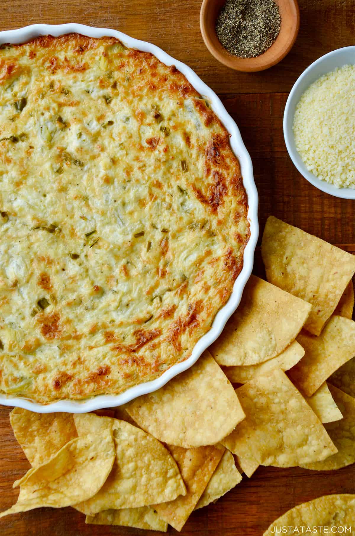 A white baking dish containing warm artichoke dip surrounded by tortilla chips.
