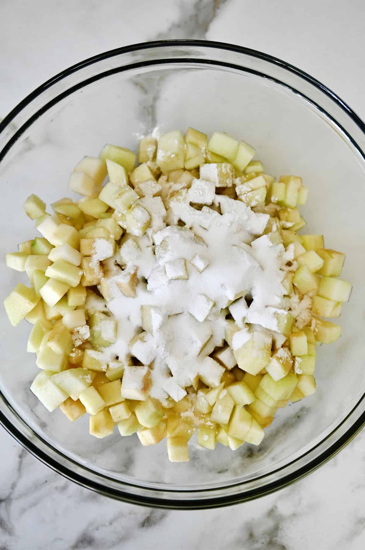 Diced apples and pears covered with flour, sugar and lemon juice in a glass bowl.