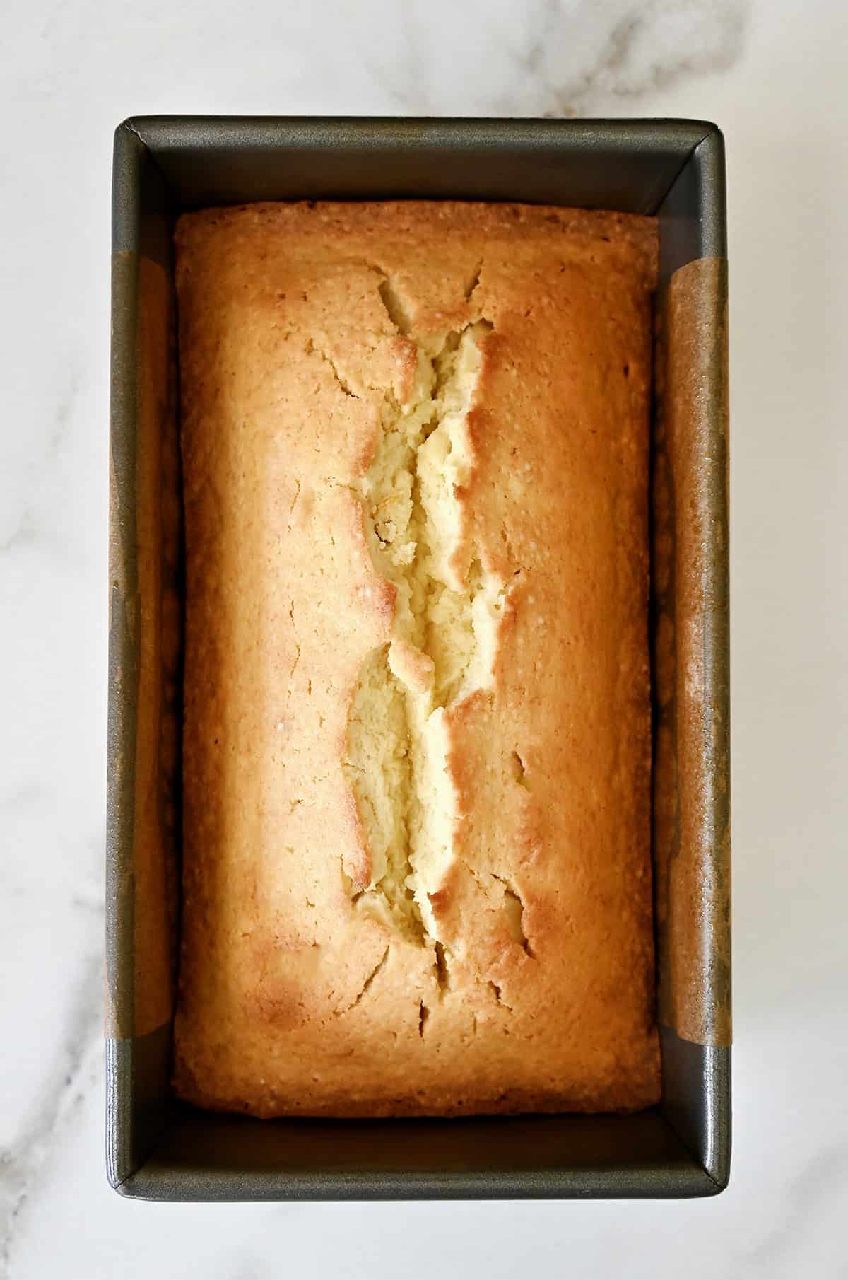 Golden brown pound cake in a loaf pan lined with parchment paper.