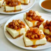 Caramel Apple Cheesecake Bars topped with sautéed apples and caramel sauce on a white serving plate.