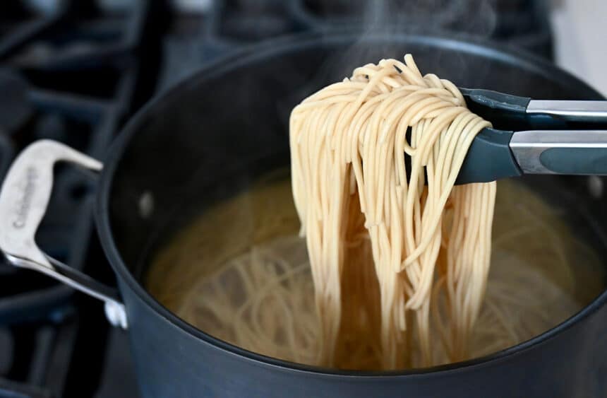Tongs holding noodles over a pot filled with water