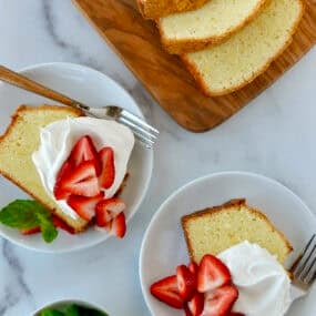 Two plates containing slices of cream cheese pound cake topped with whipped cream and fresh strawberries and garnished with fresh mint leaves.