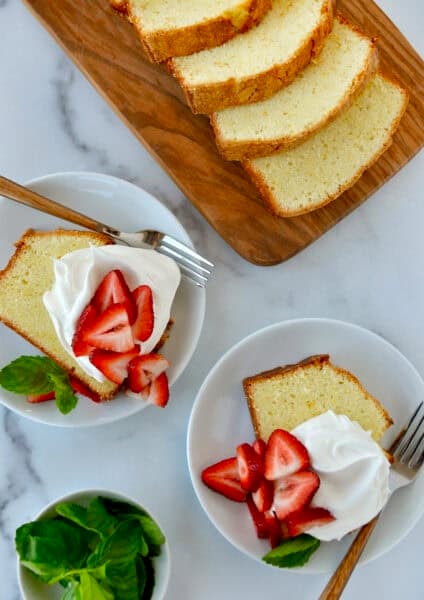 Two plates containing slices of cream cheese pound cake topped with whipped cream and fresh strawberries and garnished with fresh mint leaves.