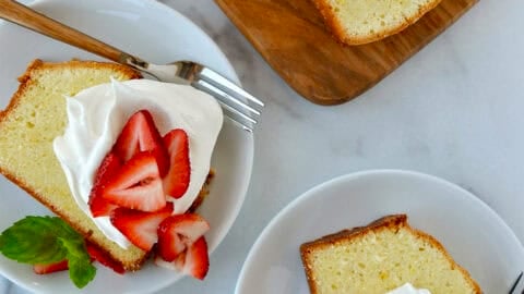 Two plates containing slices of cream cheese pound cake topped with whipped cream and fresh strawberries and garnished with fresh mint leaves.