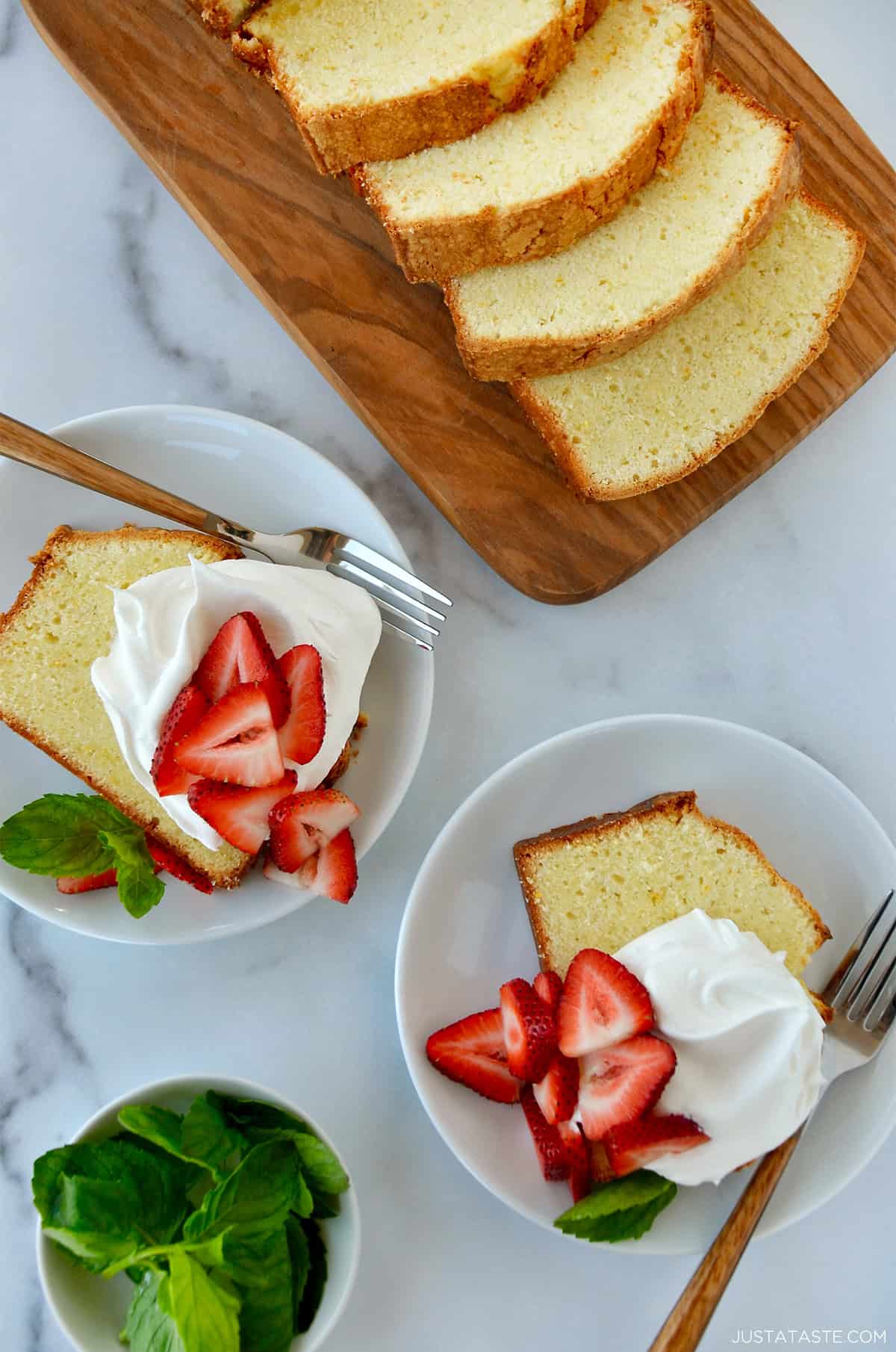Two plates containing slices of cream cheese pound cake topped with whipped cream and fresh strawberries and garnished with fresh mint leaves.
