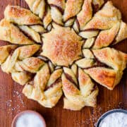 A top-down view of a Nutella Puff Pastry Snowflake next to a sifter filled with powdered sugar and a small bowl containing sanding sugar.