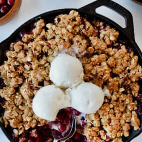 A cranberry crisp with ice cream on top and spoons sticking out