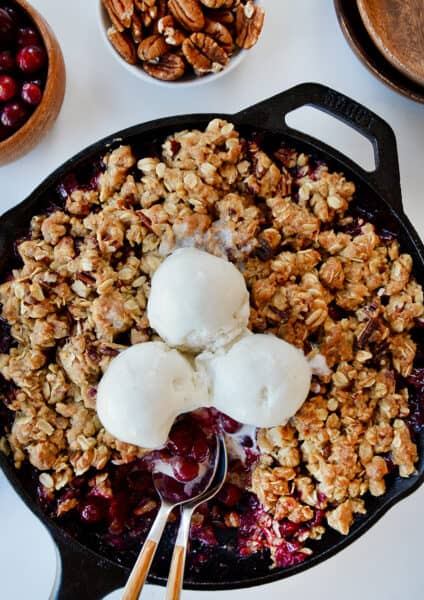 A cranberry crisp with ice cream on top and spoons sticking out