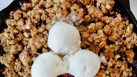 A cranberry crisp with ice cream on top and spoons sticking out