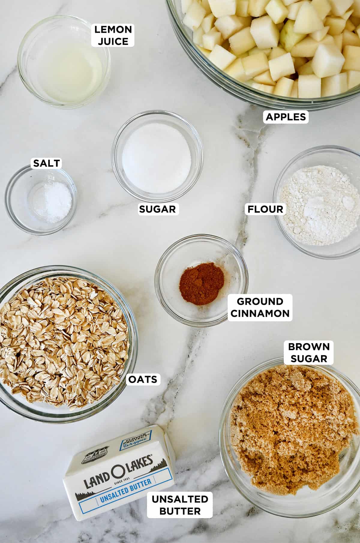 Pear crisp ingredients in glass bowls, including brown sugar, oats, flour, ground cinnamon, diced apples and pears, butter, and sugar.