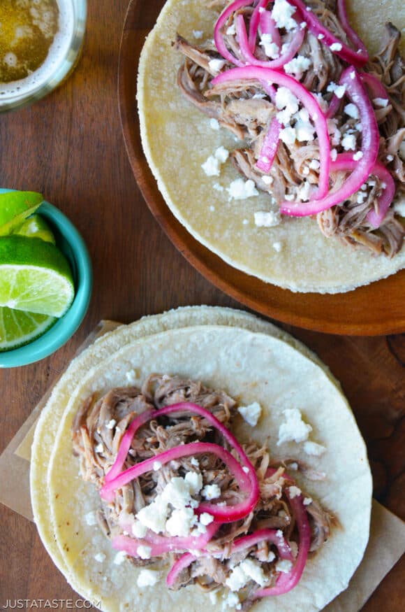 Simple Slow Cooker Pulled Pork Tacos piled high in corn tortillas and topped off with pickled onions and crumbled Cotija cheese