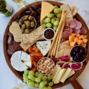 A top down view of a charcuterie board filled with meat, cheese, fruit and crackers next to glasses filled with white wine.