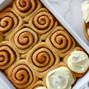 Homemade Cinnamon Rolls topped with cream cheese frosting in a white baking dish