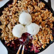 A cranberry crisp topped with three scoops of vanilla ice cream and spoons sticking out.