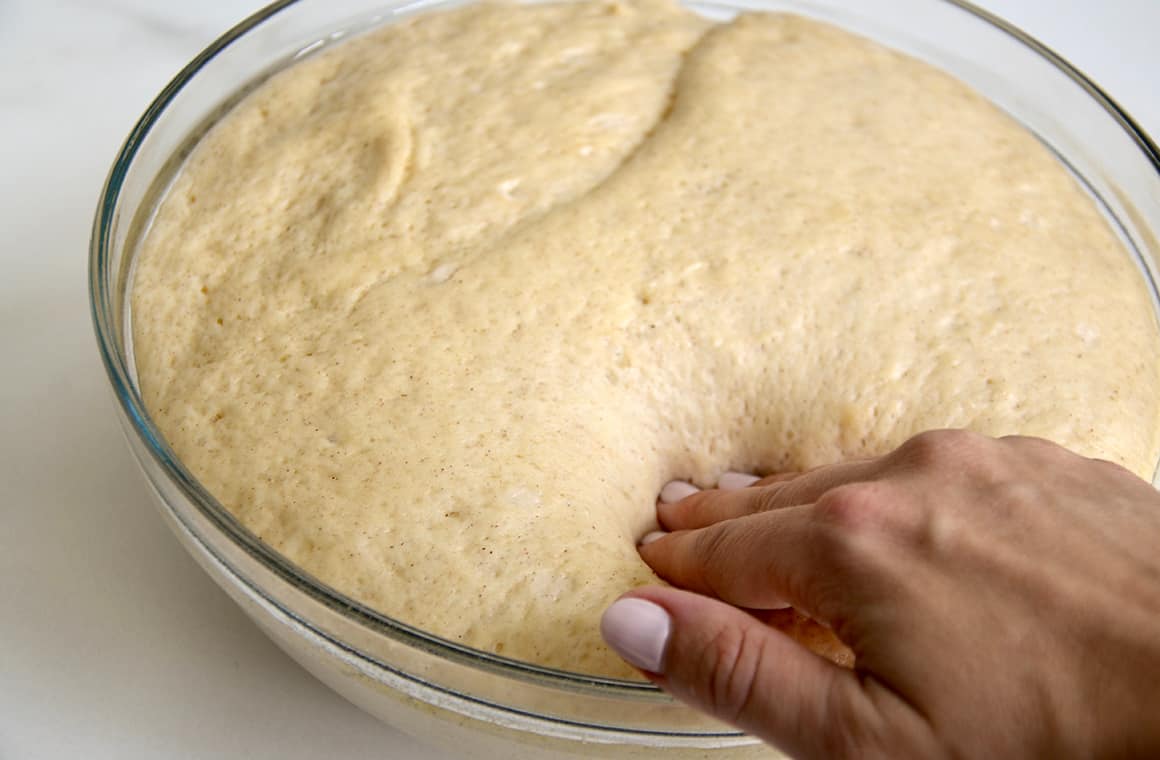 A hand pressing into proofed dough in a glass bowl