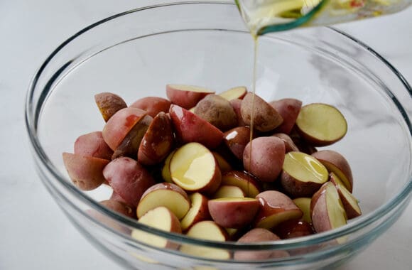 A glass bowl containing halved potatoes with olive oil