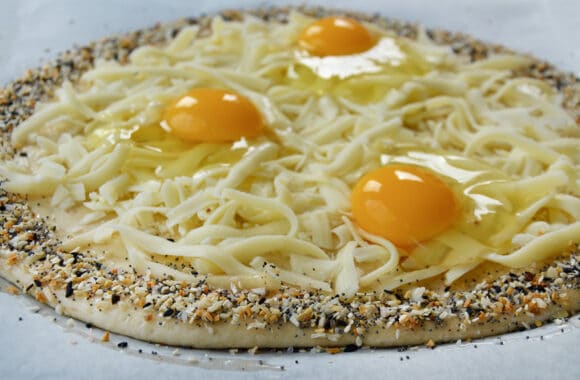 Unbaked dough topped with shredded mozzarella cheese and eggs