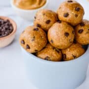 A small white bowl piled high with Peanut Butter Protein Balls studded with mini chocolate chips.