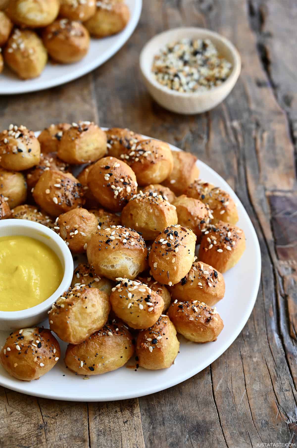 Pretzel bites with everything but the bagel seasoning on a serving plate with a small bowl containing mustard.