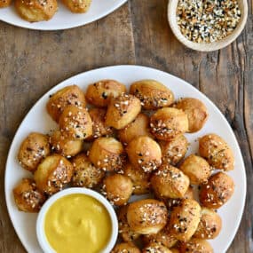 Pizza dough bites with everything seasoning on a white plate with a small bowl containing yellow mustard.