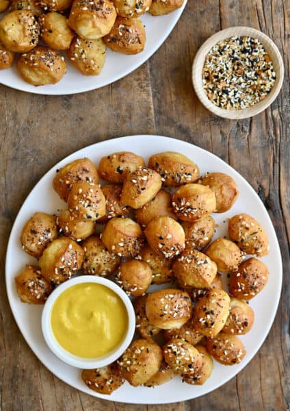 Pizza dough bites with everything seasoning on a white plate with a small bowl containing yellow mustard.