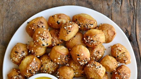 Pizza dough bites with everything seasoning on a white plate with a small bowl containing yellow mustard.