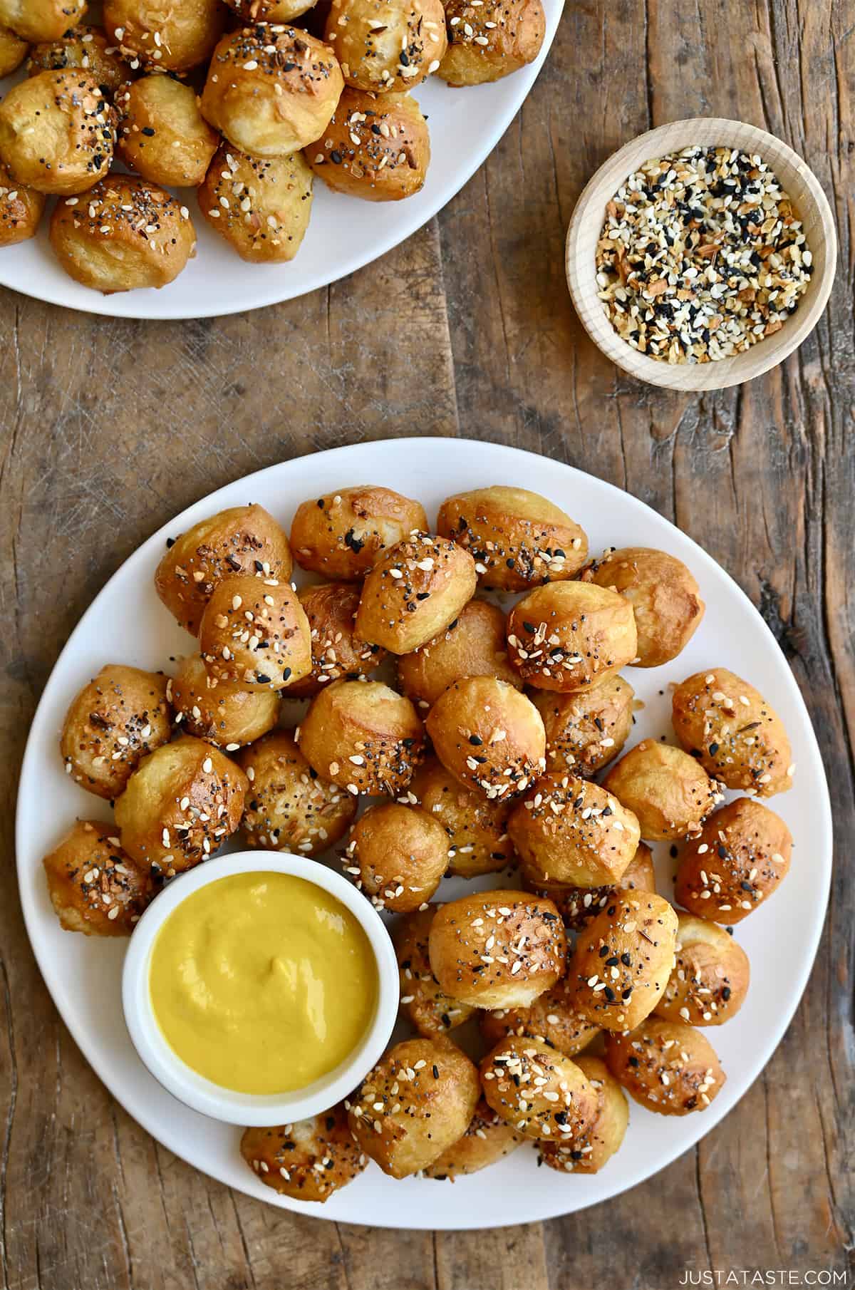 Pizza dough bites with everything seasoning on a white plate with a small bowl containing yellow mustard.