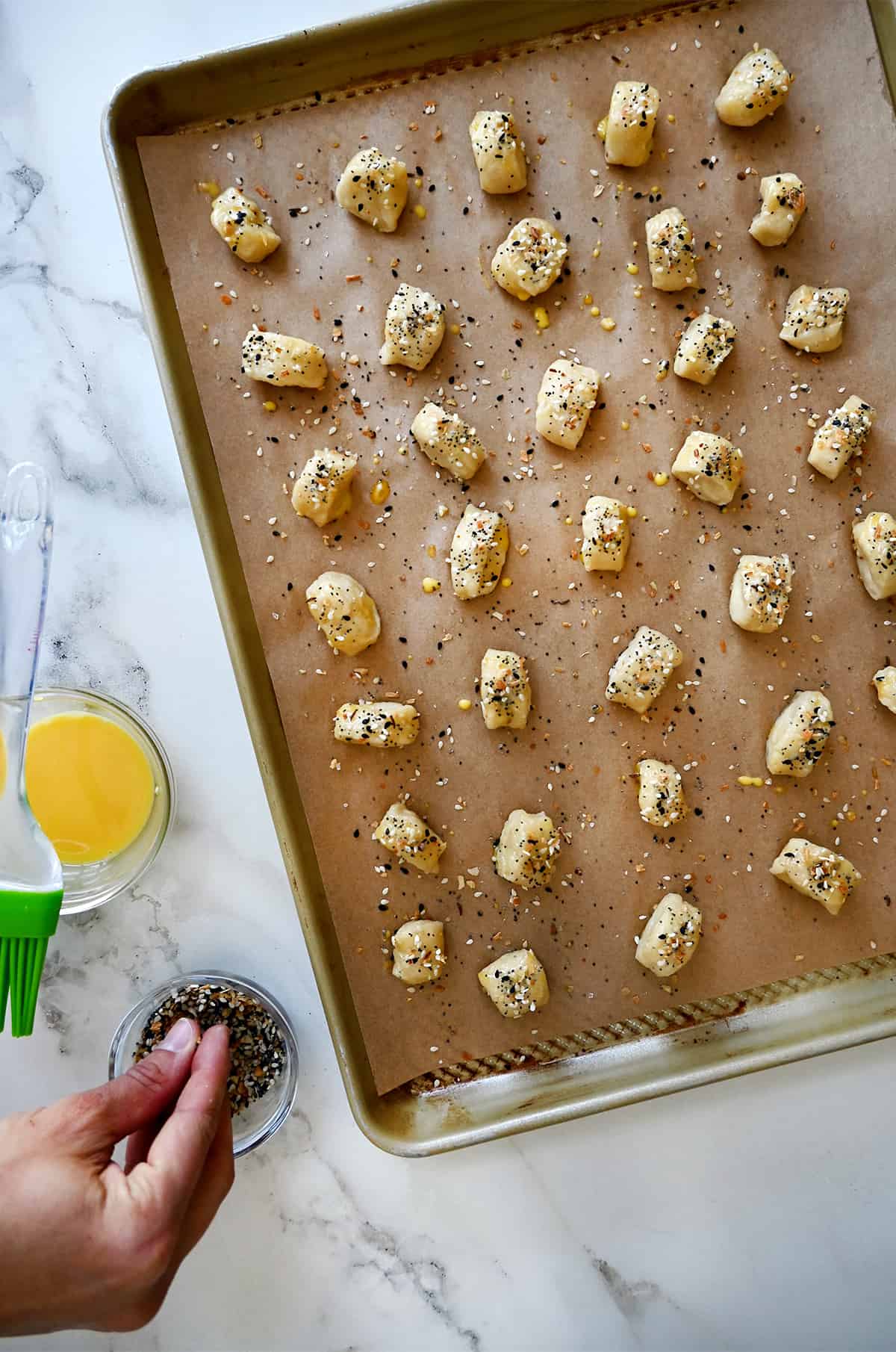 Unbaked dough pieces sprinkled with everything but the bagel seasoning on a parchment paper-lined baking sheet.