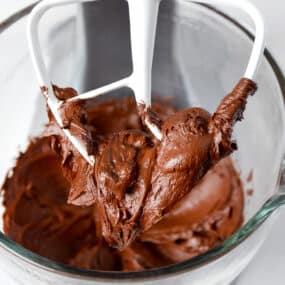 Chocolate buttercream frosting on the paddle attachment of a stand mixer.