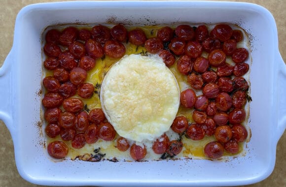 A wheel of baked Brie with tomatoes and thyme