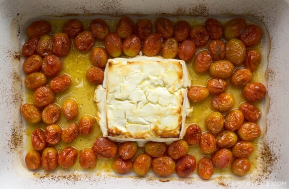 A block of baked feta cheese surrounded by roasted cherry tomatoes