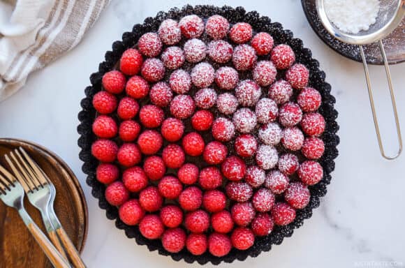 Top-down view of Easy No-Bake Chocolate Tart with Raspberries half dusted with powdered sugar next to small plates with forks