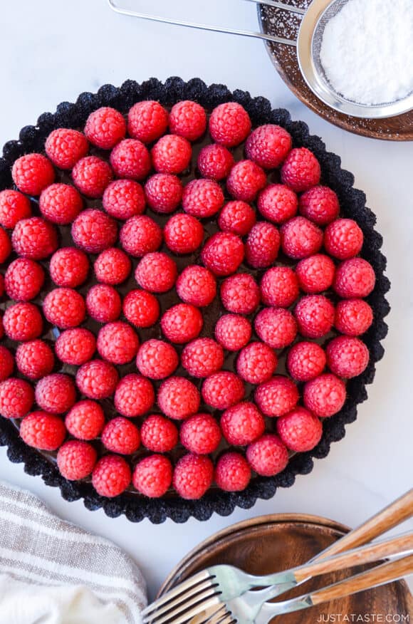 Top-down view of Easy No-Bake Chocolate Tart with Raspberries next to small plates with forks 