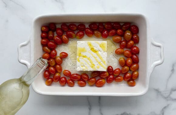 Feta cheese in a baking dish with white wine being poured in