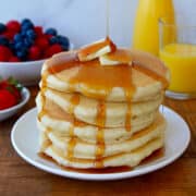 Tall stack of Fluffy Buttermilk Pancakes drizzled with maple syrup